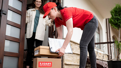 Delivery person in red uniform placing boxes labeled "Fragile" at a customer's doorstep, highlighting Smart Penny Moving's packing supplies delivery service.